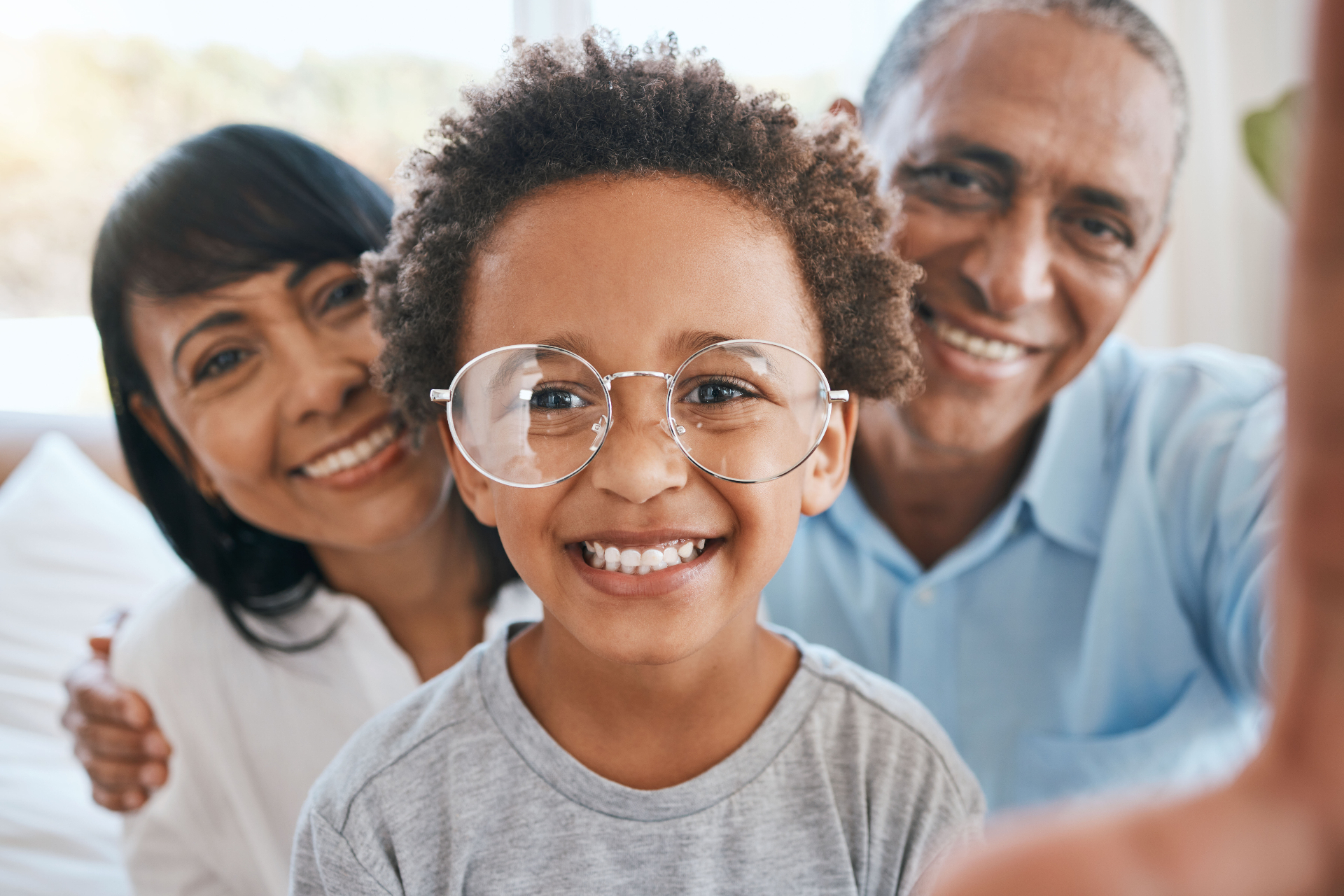 Família de três gerações sorrindo — criança de óculos de grau ao lado dos avós — Programa Assinatura Ocular Visão Fixa